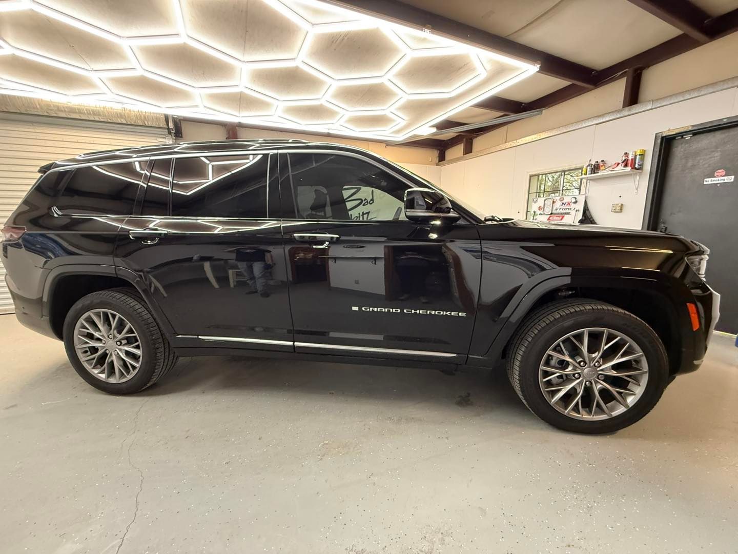 A black Jeep Grand Cherokee L parked inside a garage with hexagonal ceiling lights.