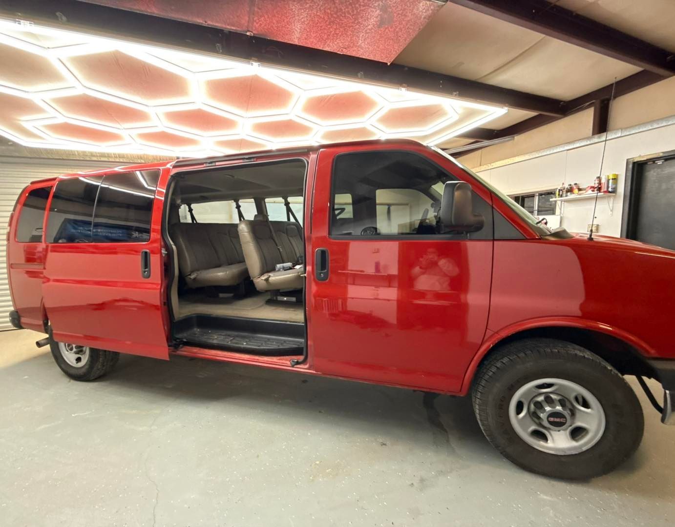A bright red passenger van with its sliding side door open, parked inside a garage with hexagonal ceiling lighting.