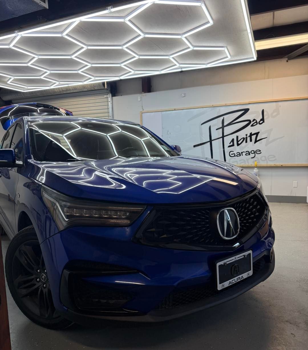 A blue Acura SUV parked inside a garage with hexagonal ceiling lights and a 