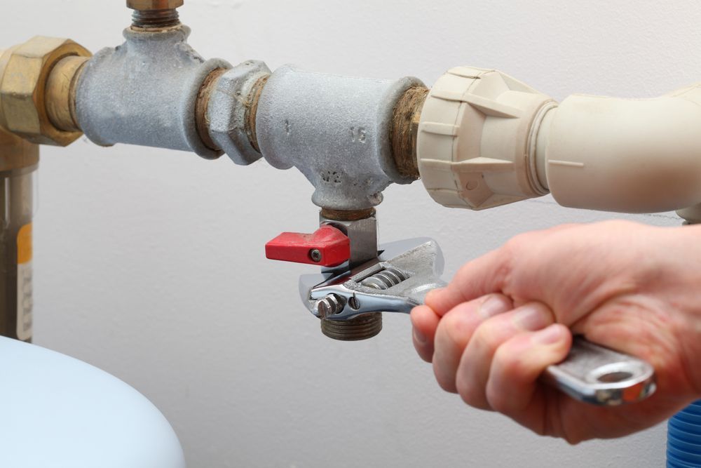Hand using a wrench to tighten a valve on a pipe, in a white-walled room. — Darwin Plumbing Maintenance in Knuckey Lagoon, NT