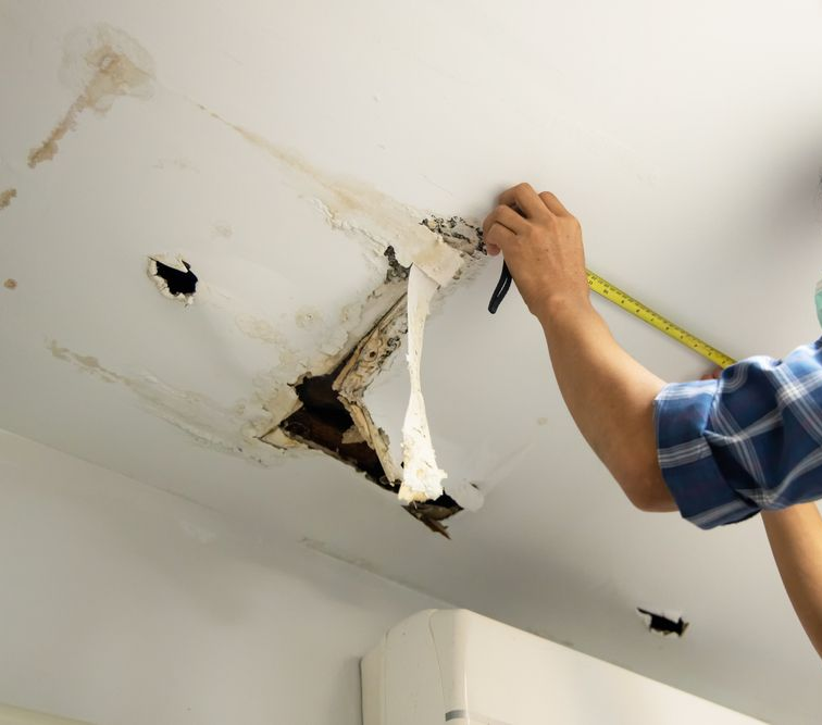 Person Measuring Water-Damaged Ceiling With a Hole — Darwin Plumbing Maintenance in Knuckey Lagoon, NT