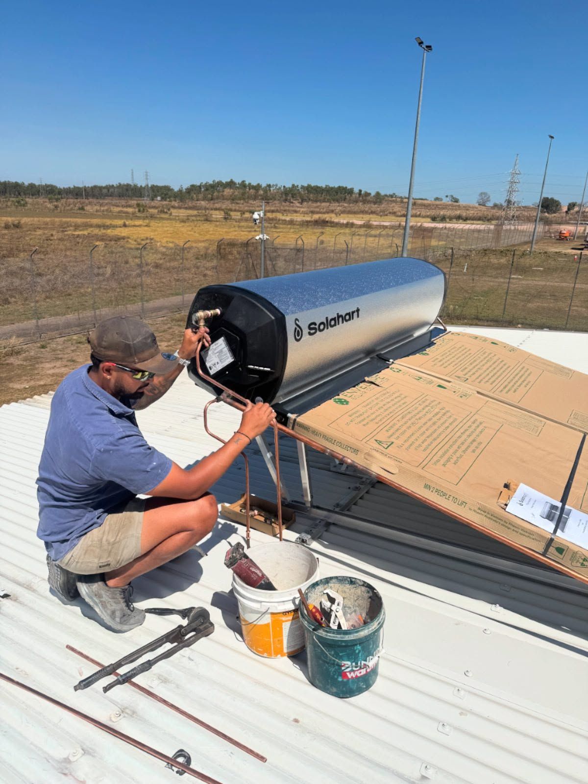 Man installing a solar water heater on a rooftop under a blue sky. — Darwin Plumbing Maintenance in Knuckey Lagoon, NT