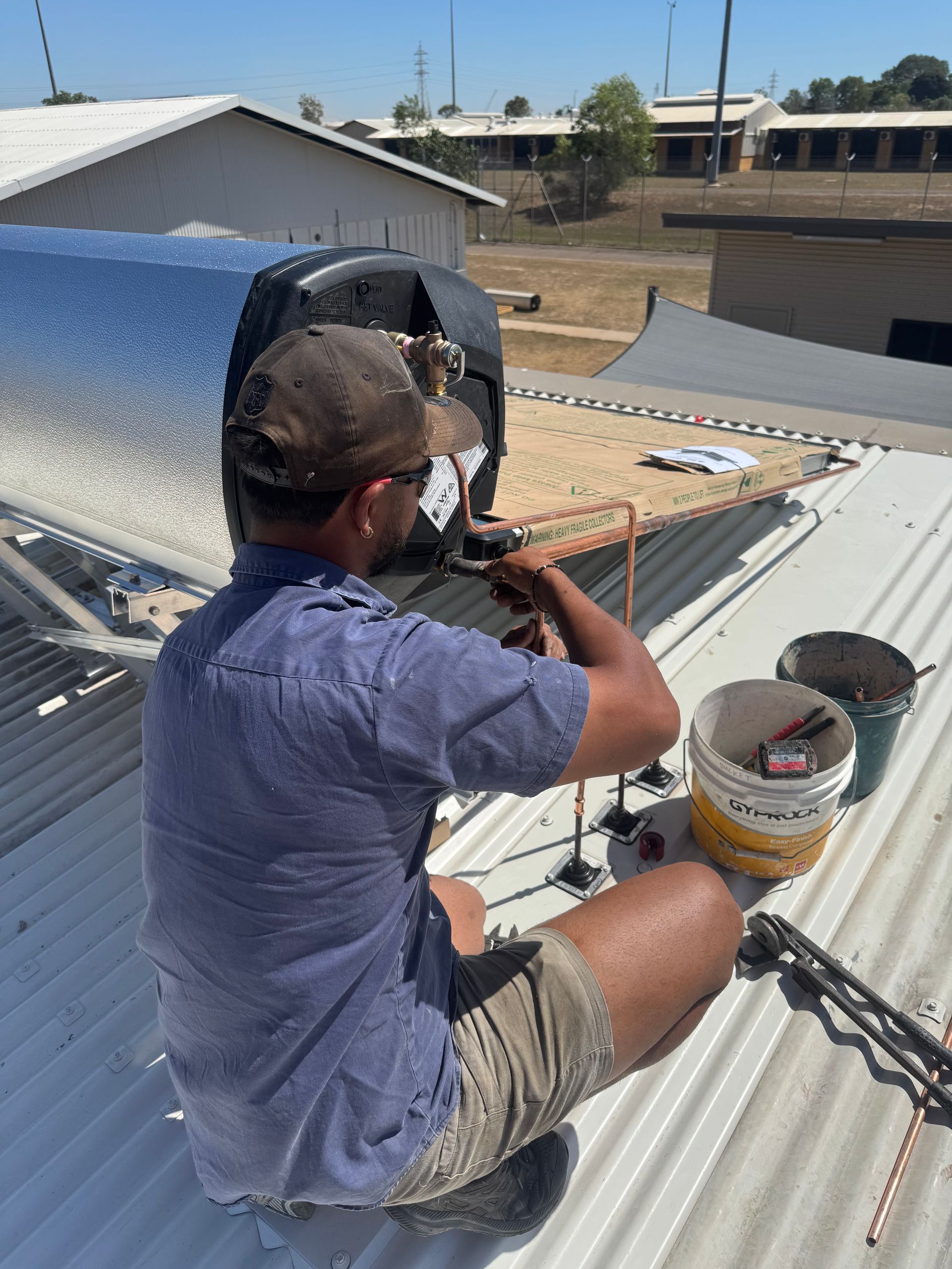 Man in hat works on rooftop solar panel, sunny day. — Darwin Plumbing Maintenance in Knuckey Lagoon, NT