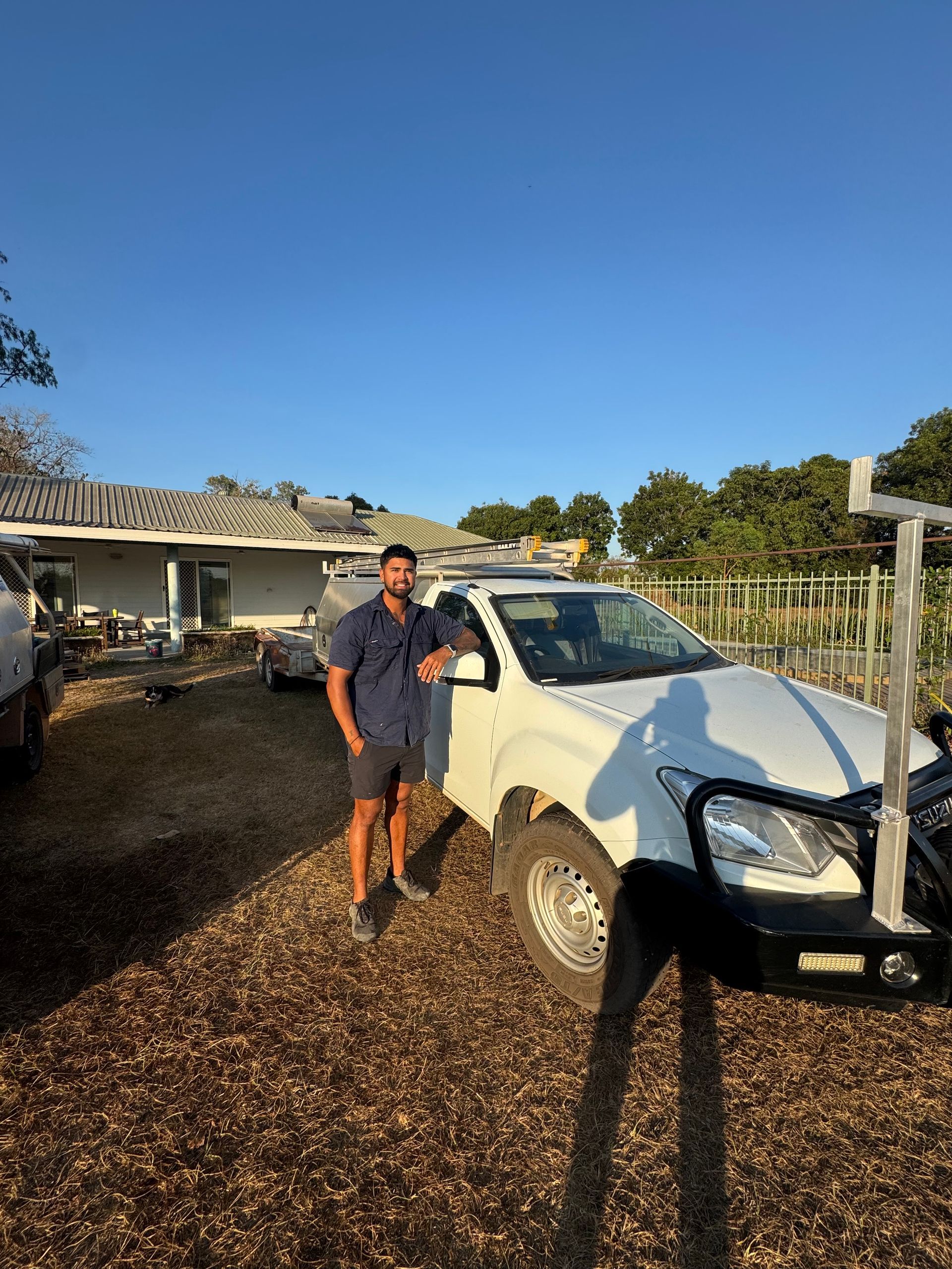 Man in work clothes leans on white truck, in front of a house, under a blue sky. — Darwin Plumbing Maintenance in Knuckey Lagoon, NT