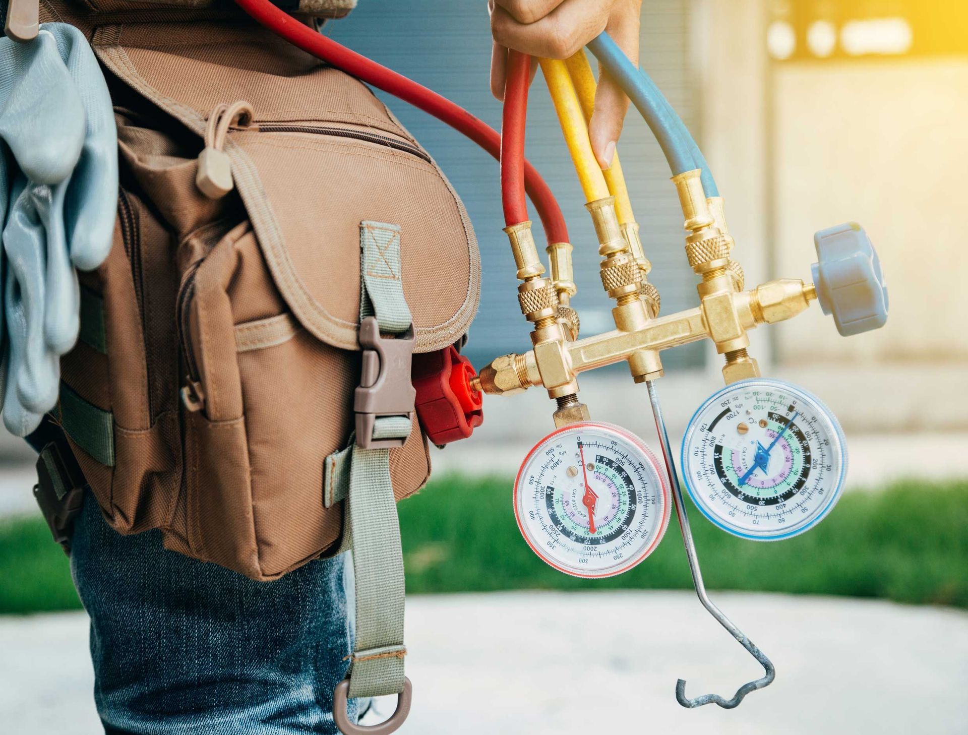 Technician holding gauges and hoses for HVAC repair, wearing a tool belt.