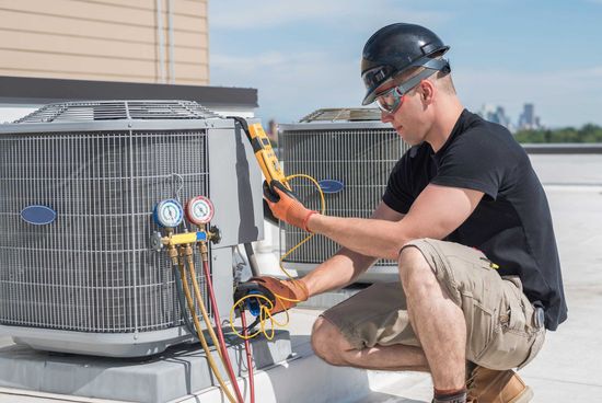 HVAC technician inspects rooftop air conditioning unit, using a meter and gauges. HVAC technician inspects rooftop air conditioning unit, using a meter and gauges.