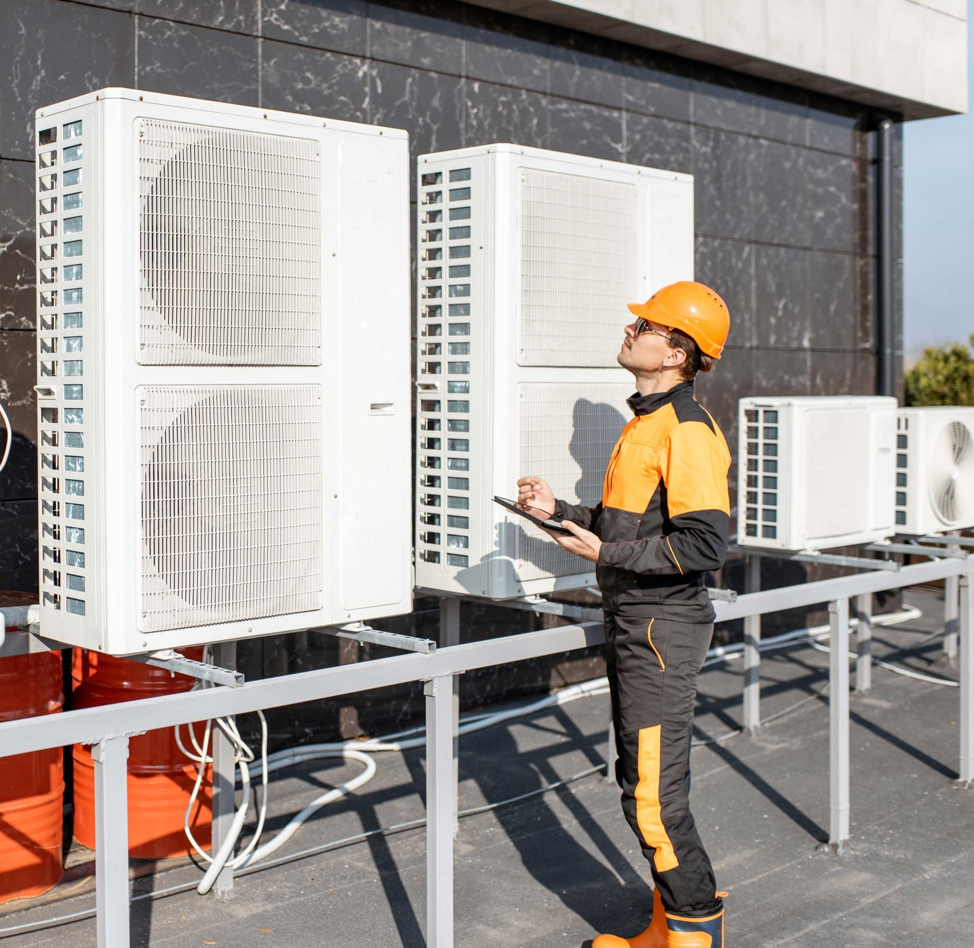 HVAC technician in orange safety gear inspecting rooftop air conditioning units.