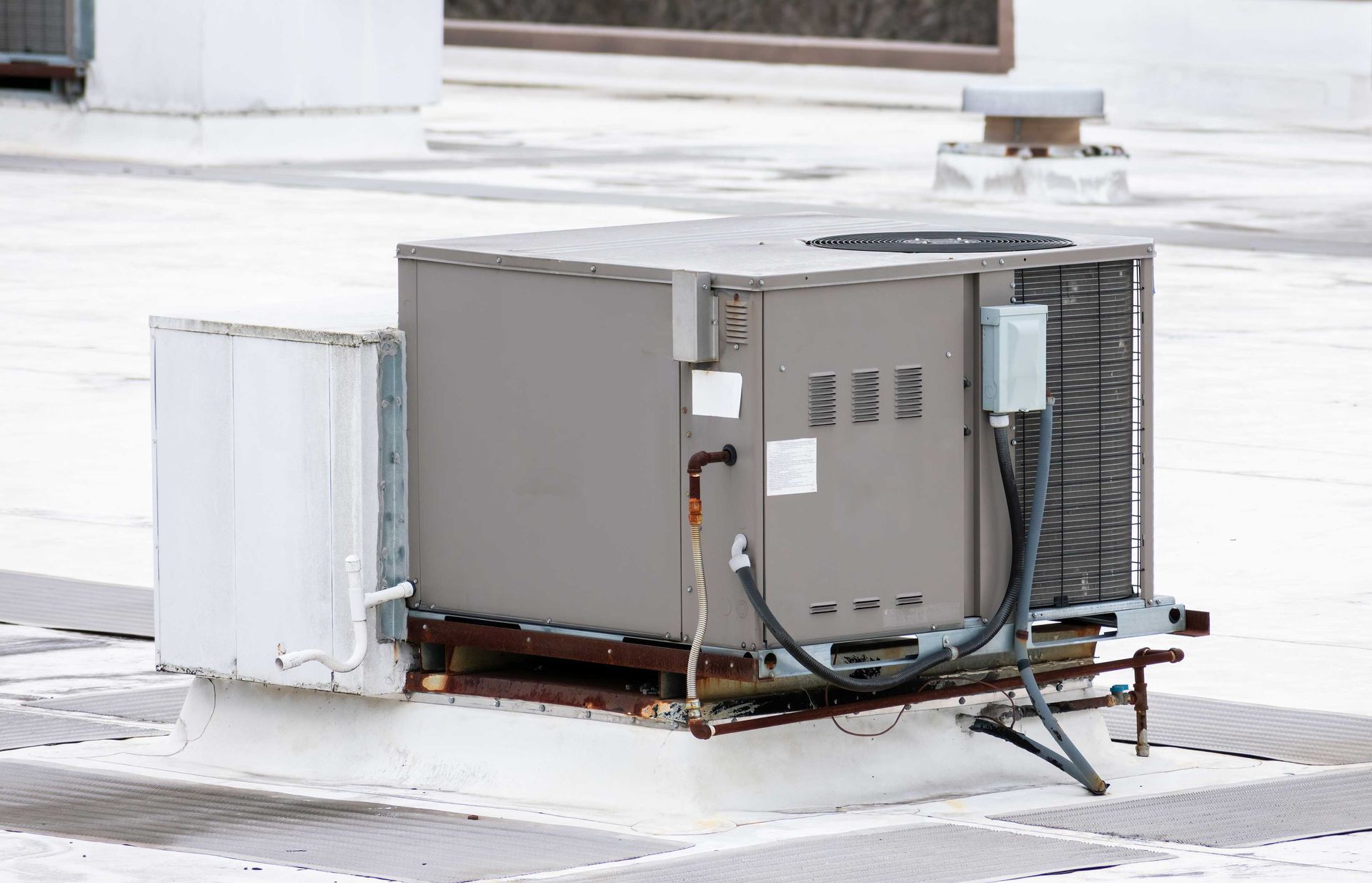 Rooftop HVAC unit, gray metal box with fan, electrical conduit, on white roof.