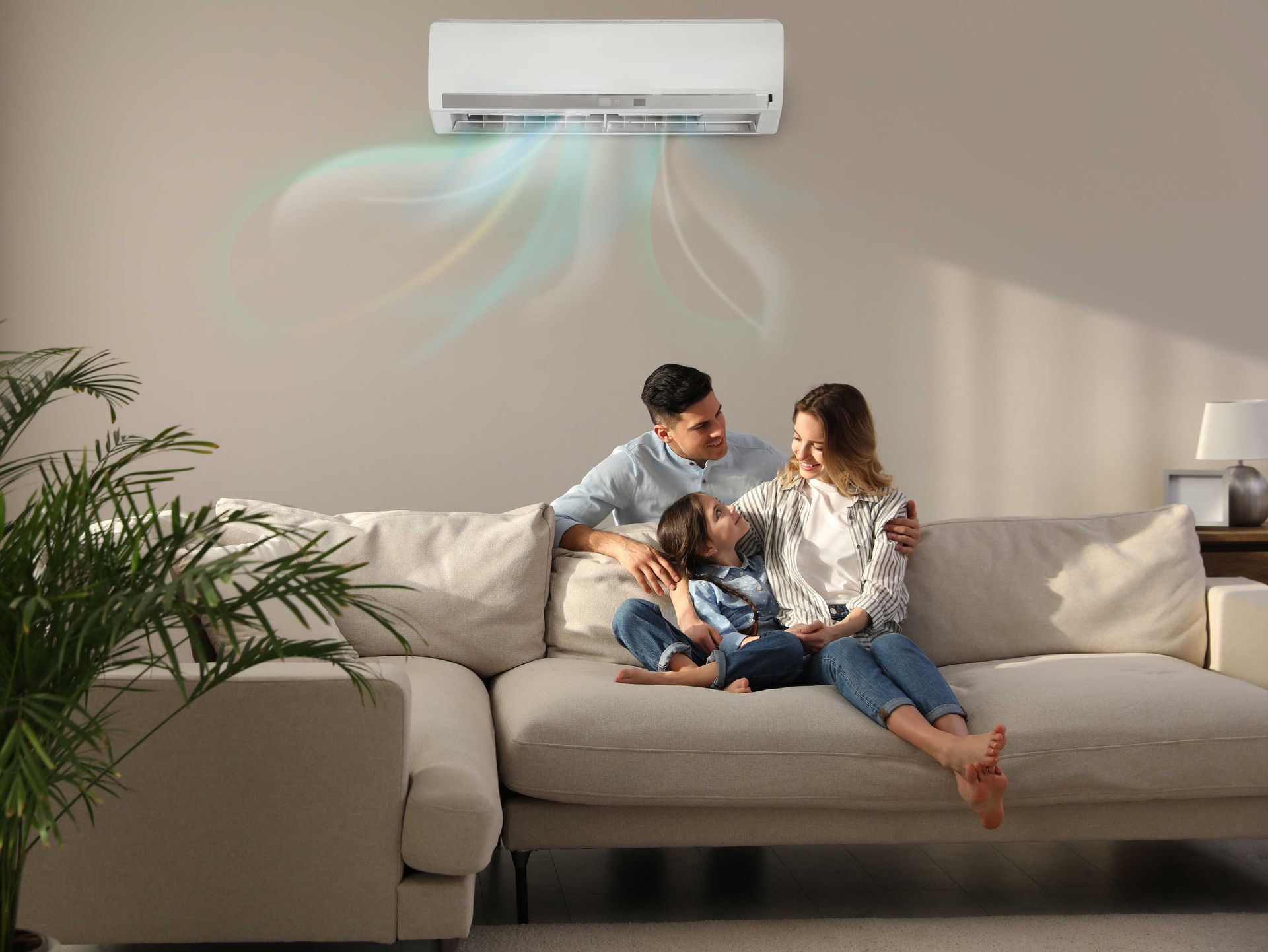 Family sitting on a sofa, under an air conditioner, in a light-colored living room.