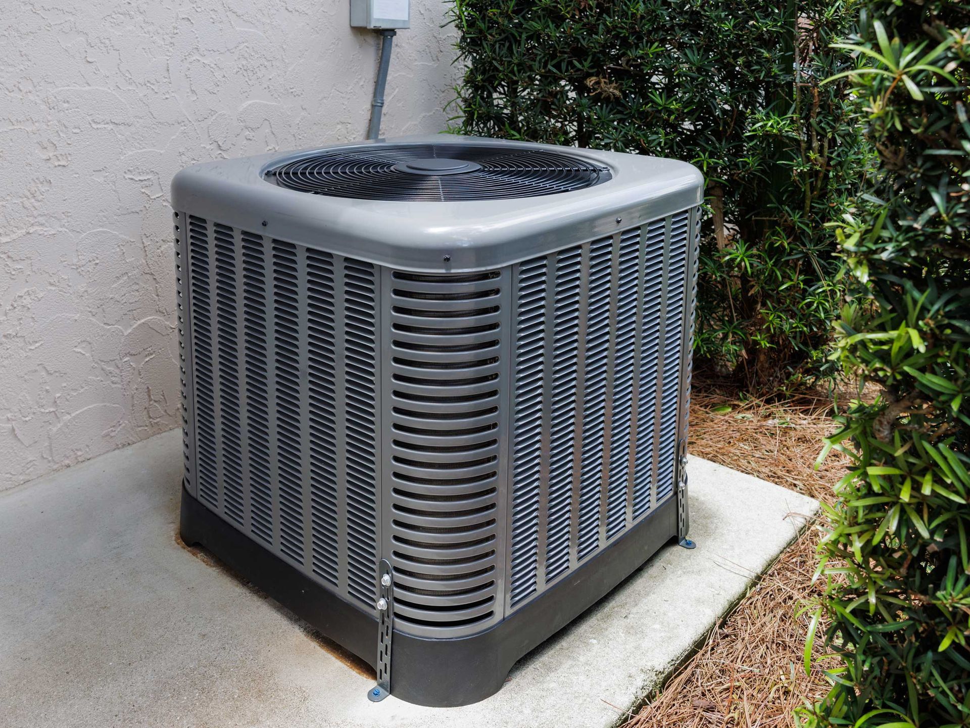 Gray outdoor air conditioning unit on a concrete pad near foliage.