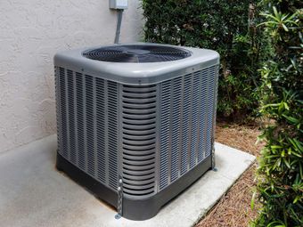 Gray outdoor air conditioning unit on a concrete pad near foliage. Gray outdoor air conditioning unit on a concrete pad near foliage.