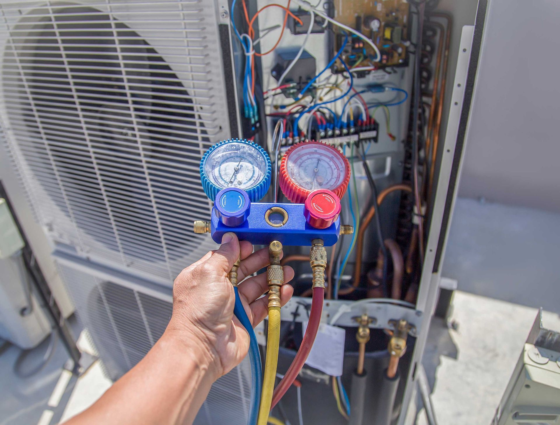 A person servicing an air conditioning unit, using gauges and hoses.