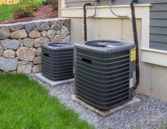 Two outdoor air conditioning units on concrete pads near a stone wall and house siding. Two outdoor air conditioning units on concrete pads near a stone wall and house siding.
