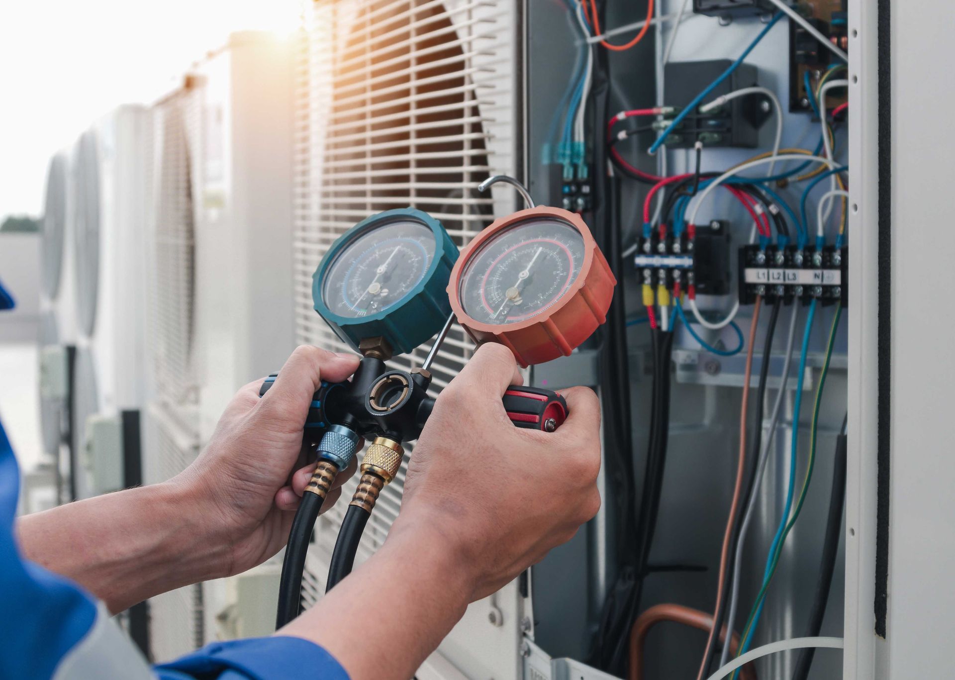 Person using gauges to check an air conditioning unit's components outdoors.