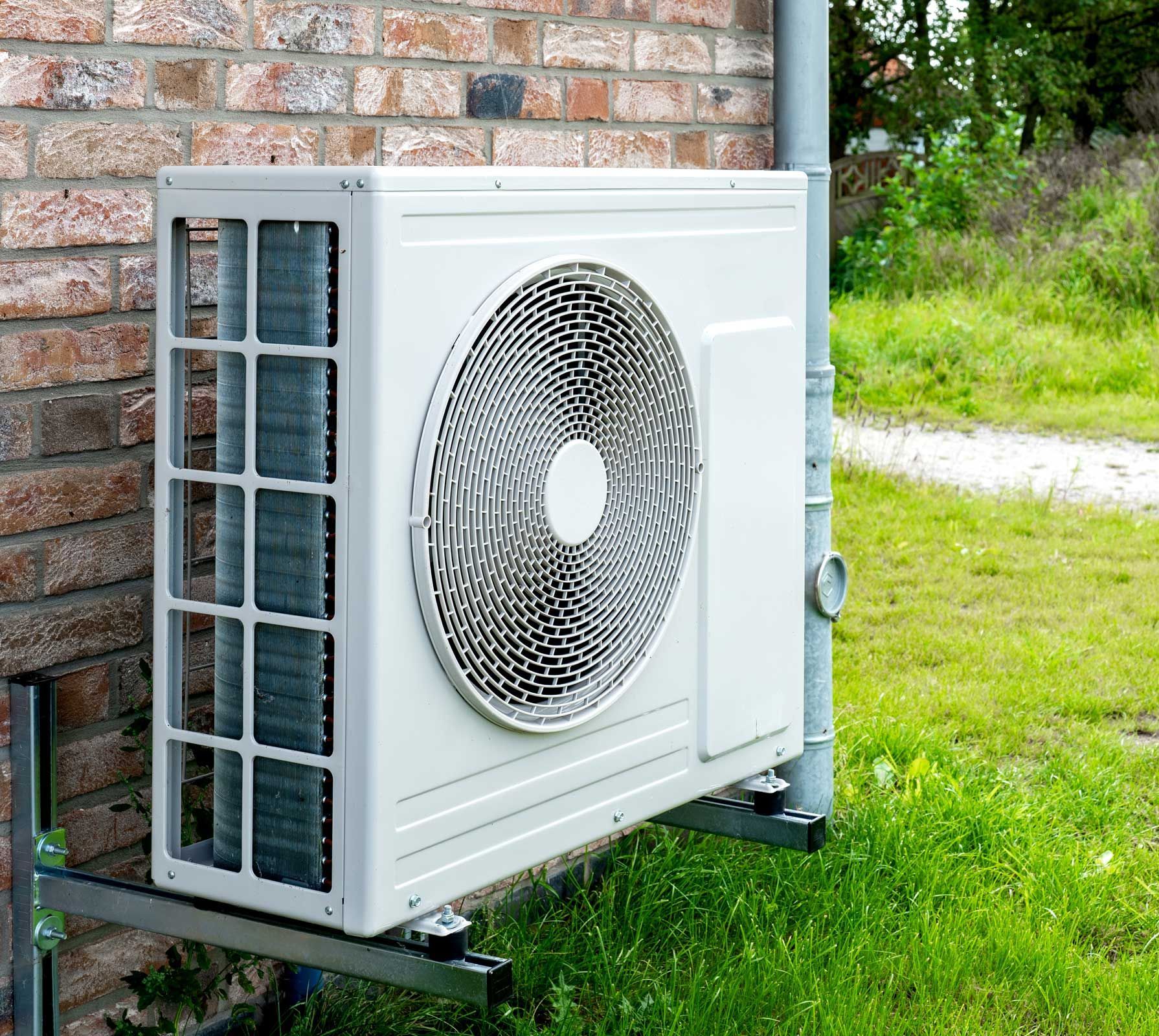 White air conditioning unit mounted on a brick wall, next to green grass.