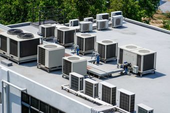 Air conditioning units on a building rooftop. Gray and white units with trees in the background. Air conditioning units on a building rooftop. Gray and white units with trees in the background.