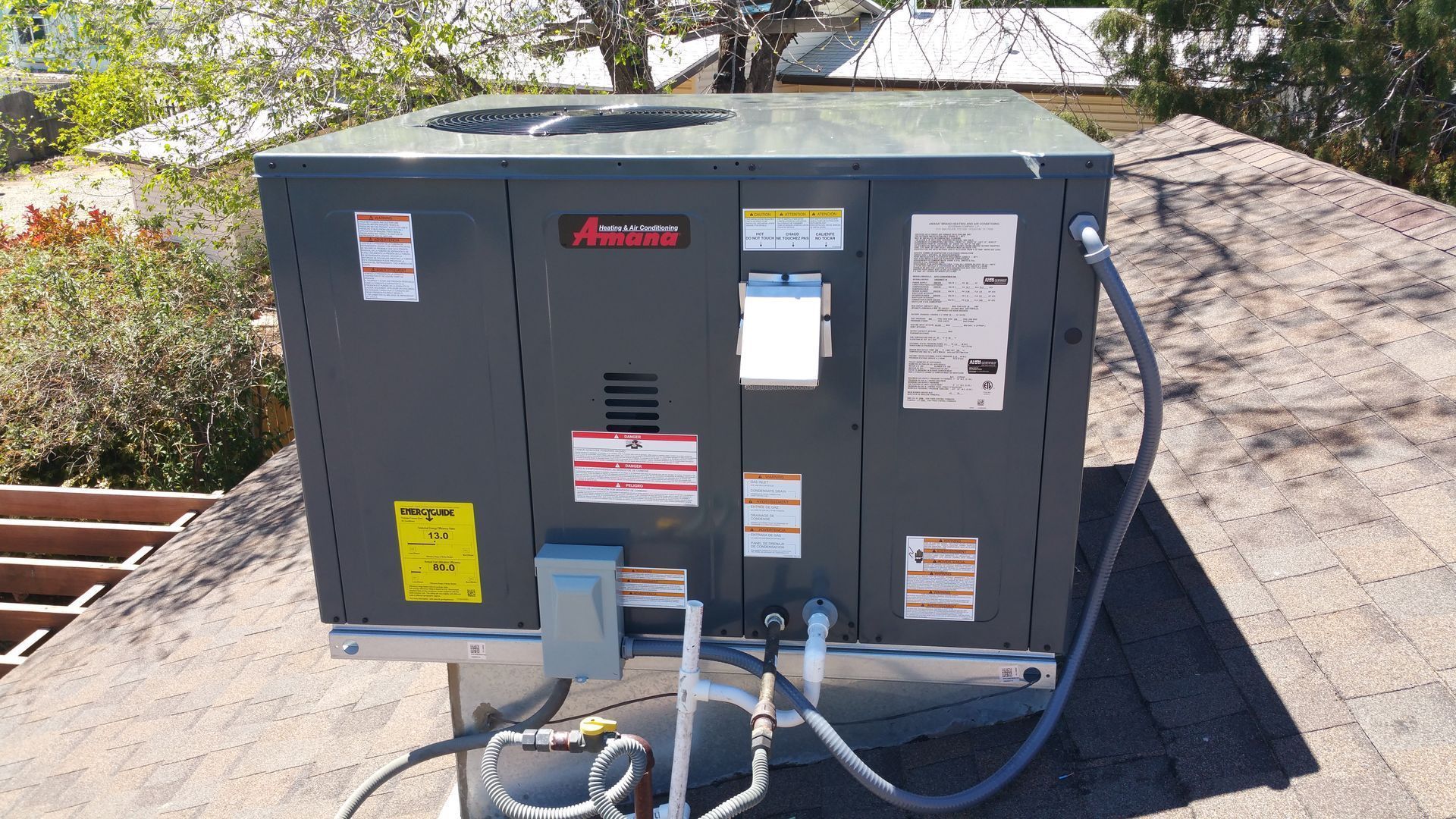 Air conditioning unit on a rooftop, gray with various labels and connected pipes and wires.