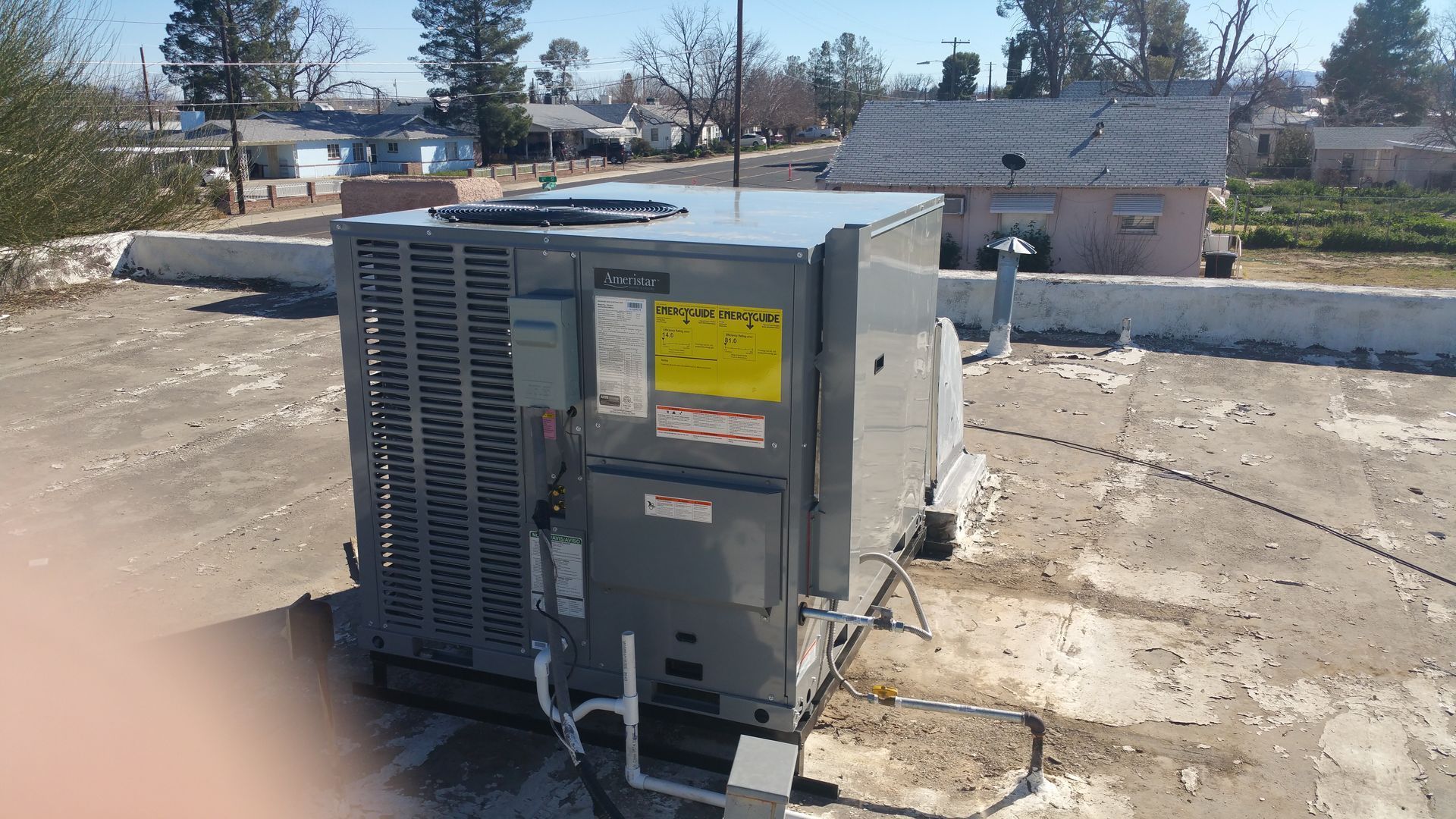 HVAC unit on a rooftop with surrounding houses and trees under a clear sky.
