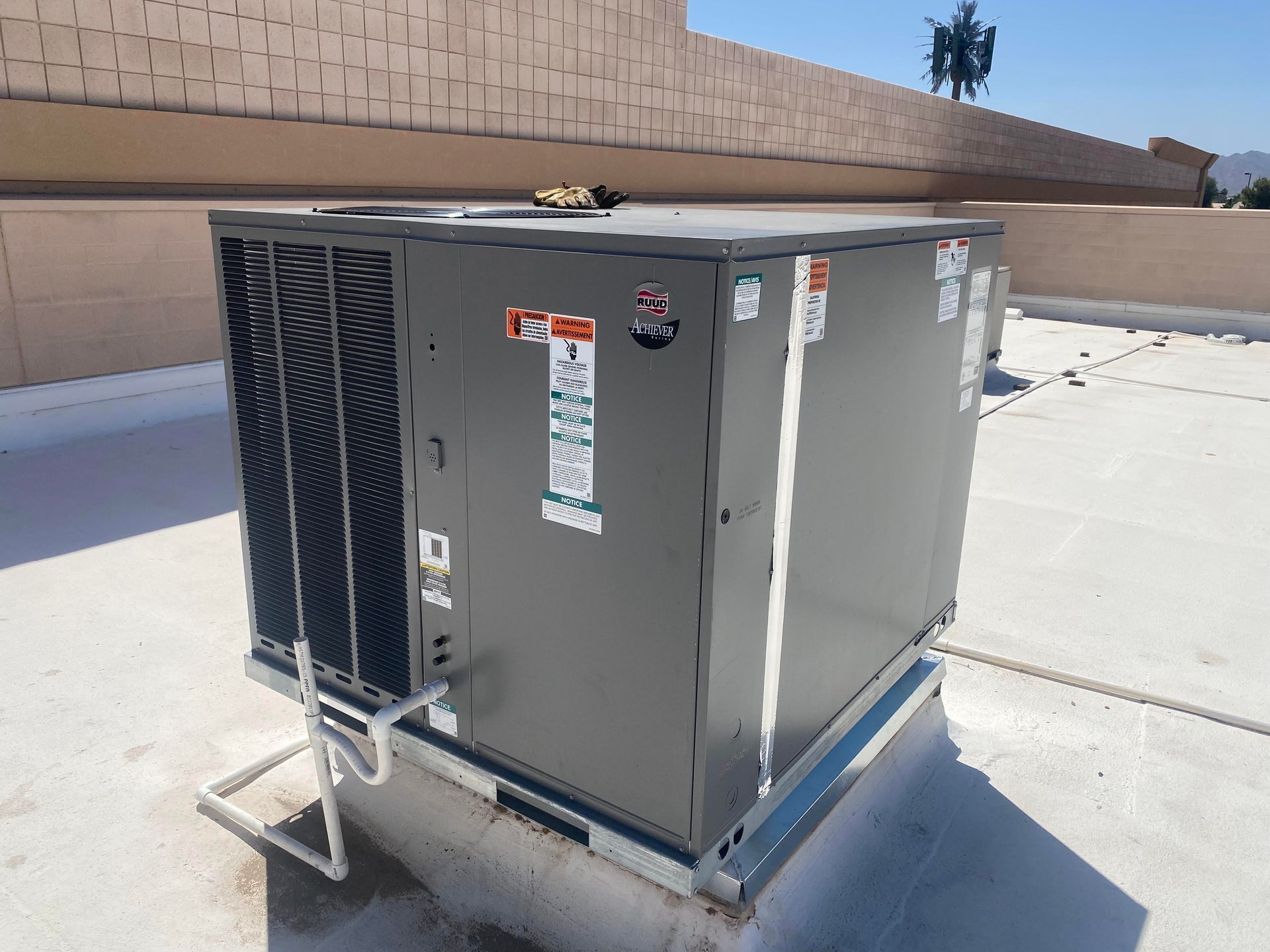 Gray rooftop air conditioning unit, mounted on a white roof, against a blue sky.