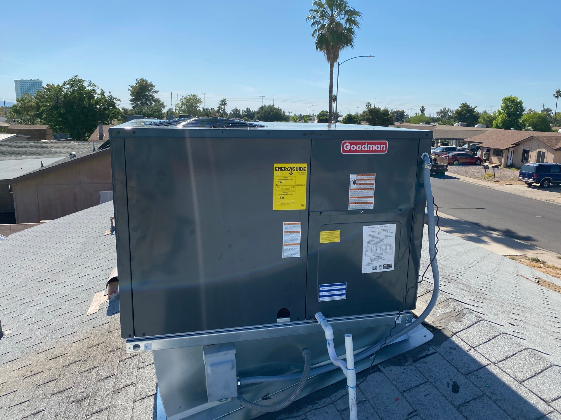 Rooftop air conditioning unit with various labels, gray, on a residential roof under a blue sky.