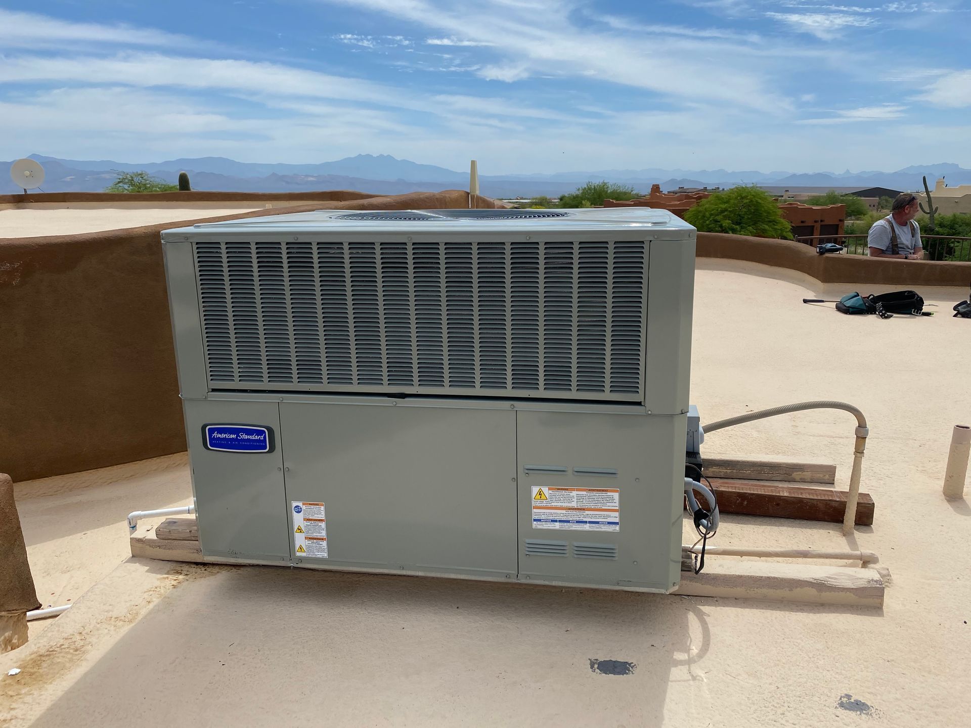 Air conditioning unit on a rooftop, with a person working in the background under a blue sky.