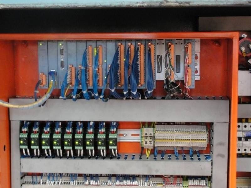 Quadro elettrico aperto con file di relè, cablaggi e moduli circuitali all'interno di un armadio metallico.