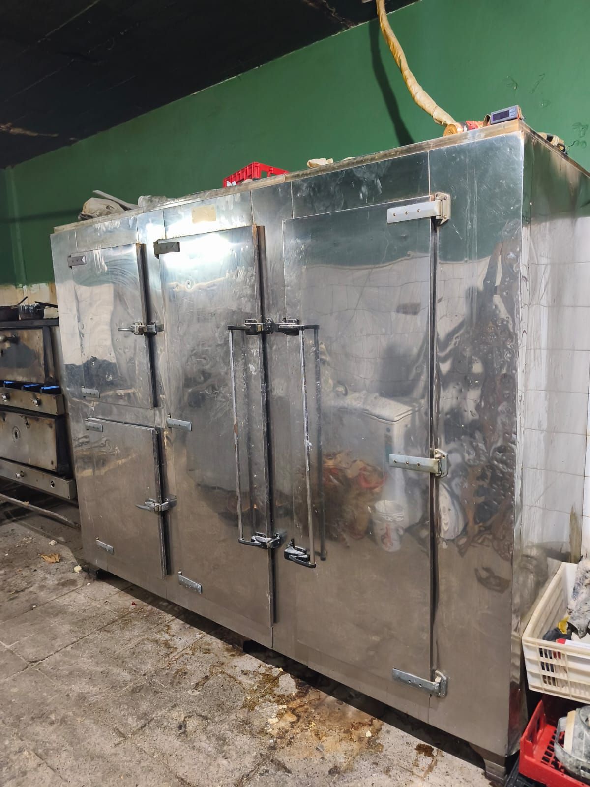 Un trabajador con guantes utiliza una máquina roja con mangueras para limpiar un suelo mojado y un desagüe.