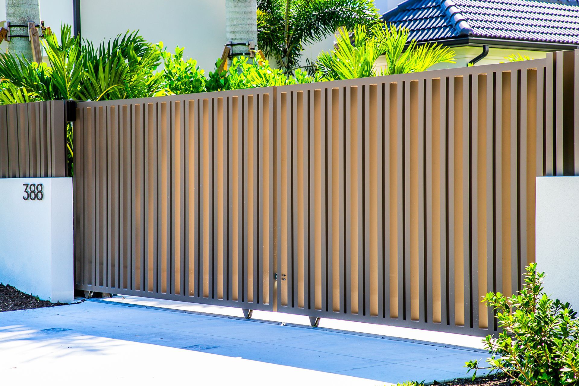 Tan slatted metal gate along a white wall in front of a bright residential home