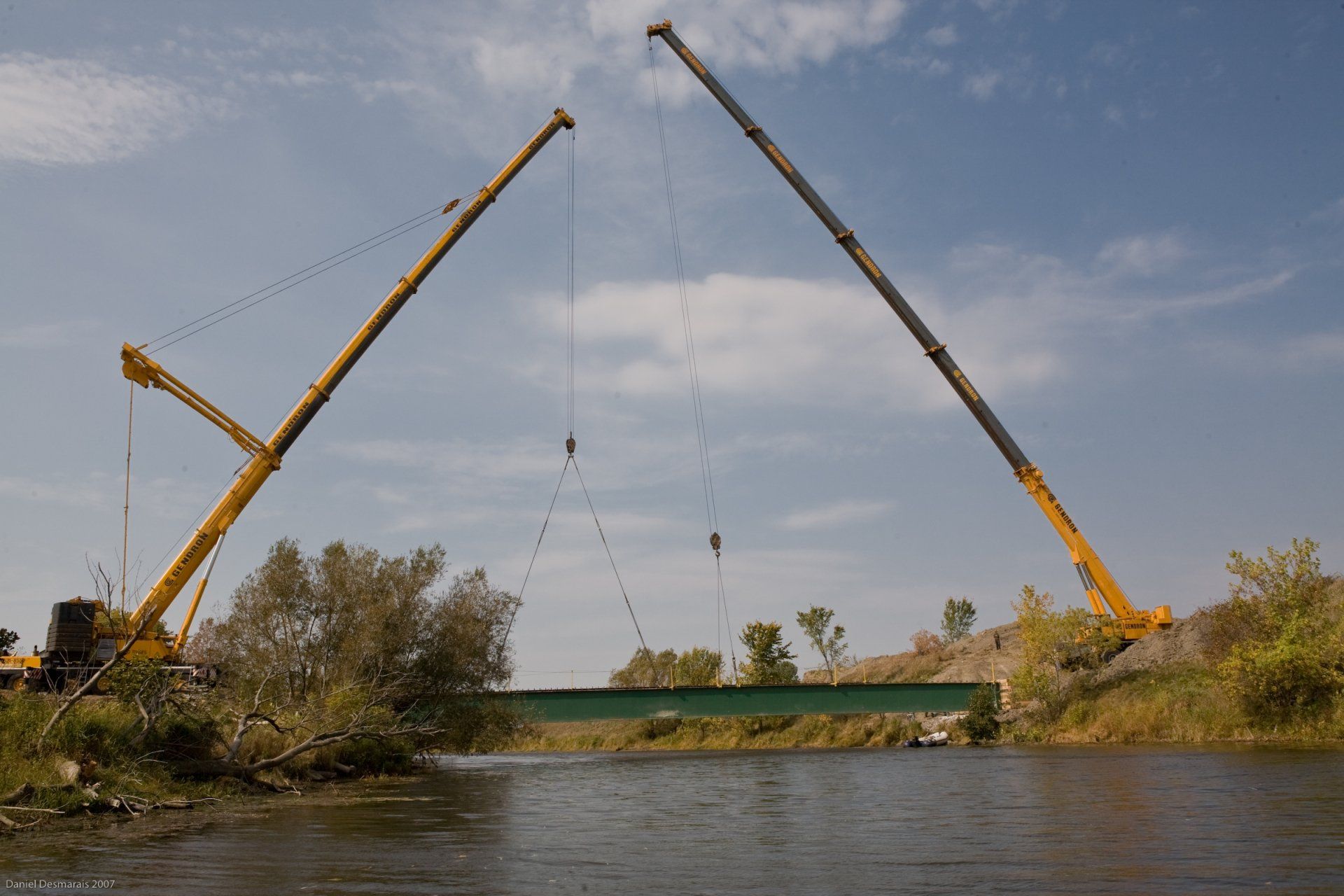 Deux grues soulèvent un pont au-dessus d'un plan d'eau