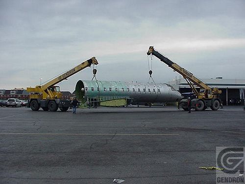 Deux grues soulèvent un gros objet dans un parking