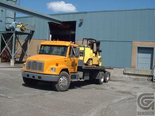 A yellow truck with a forklift on the back is parked in front of a building