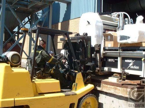 A man is driving a yellow forklift in front of a building