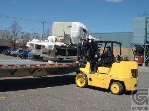 A man is driving a yellow forklift on a trailer