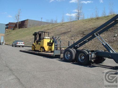 A yellow forklift is being towed by a trailer that says geroron