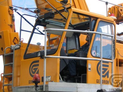 Un homme est assis sur le siège conducteur d'une grue jaune qui dit gedron