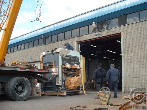 A large machine is being loaded onto a truck in front of a building