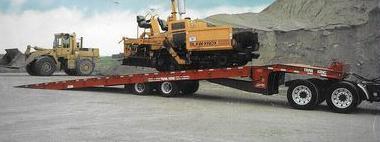 A yellow bulldozer is being towed by a red trailer.
