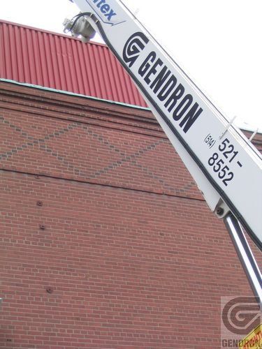 Une grue Gendron est posée au sommet d'un bâtiment en brique