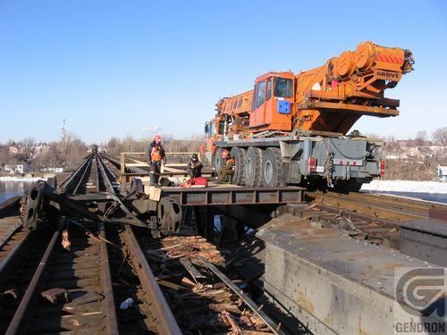 Une grande grue orange est posée au sommet d’une voie ferrée.