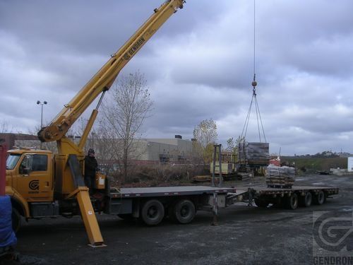 Une grande grue jaune est fixée à l'arrière d'un camion à plateau