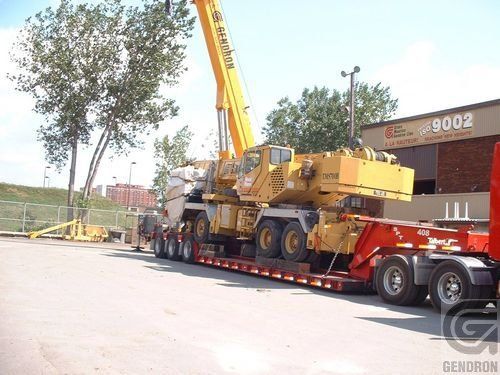Un camion avec une grue à l'arrière est garé devant un bâtiment qui indique 9002
