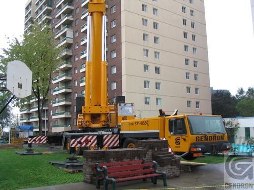 Un camion Gendron jaune est stationné devant un grand immeuble