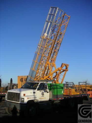 Un camion auquel est attachée une grue est garé devant un panneau indiquant genron