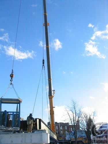 Une grue soulève une structure en béton dans les airs.