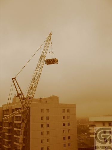 Une grande grue soulève un gros objet au-dessus d'un bâtiment