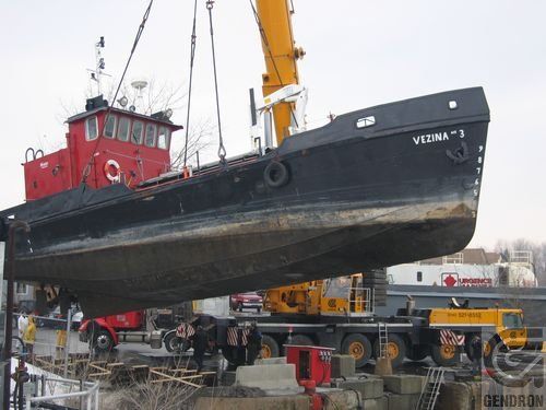 Un grand bateau portant le nom de Vizna est soulevé par une grue