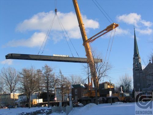 Une grande grue soulève un gros morceau de métal dans la neige près d'une église