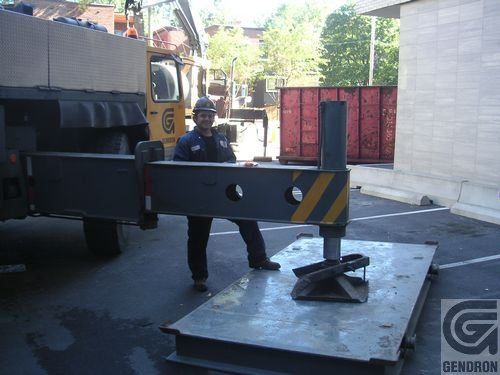 Un homme se tient à côté d’un morceau de métal sur lequel est écrit Denaron.