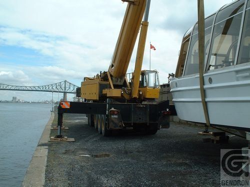 Un bateau est soulevé par une grande grue jaune qui indique Genoron au fond