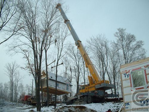 Une grande grue jaune soulève une maison dans la neige